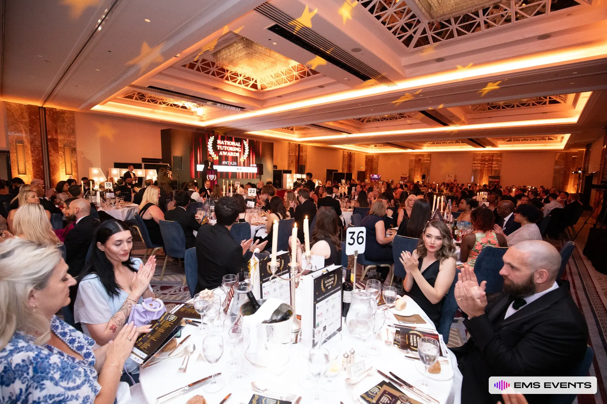 Guests applauding during the 5th National Tutoring Awards ceremony with the #NTA26 stage backdrop visible behind