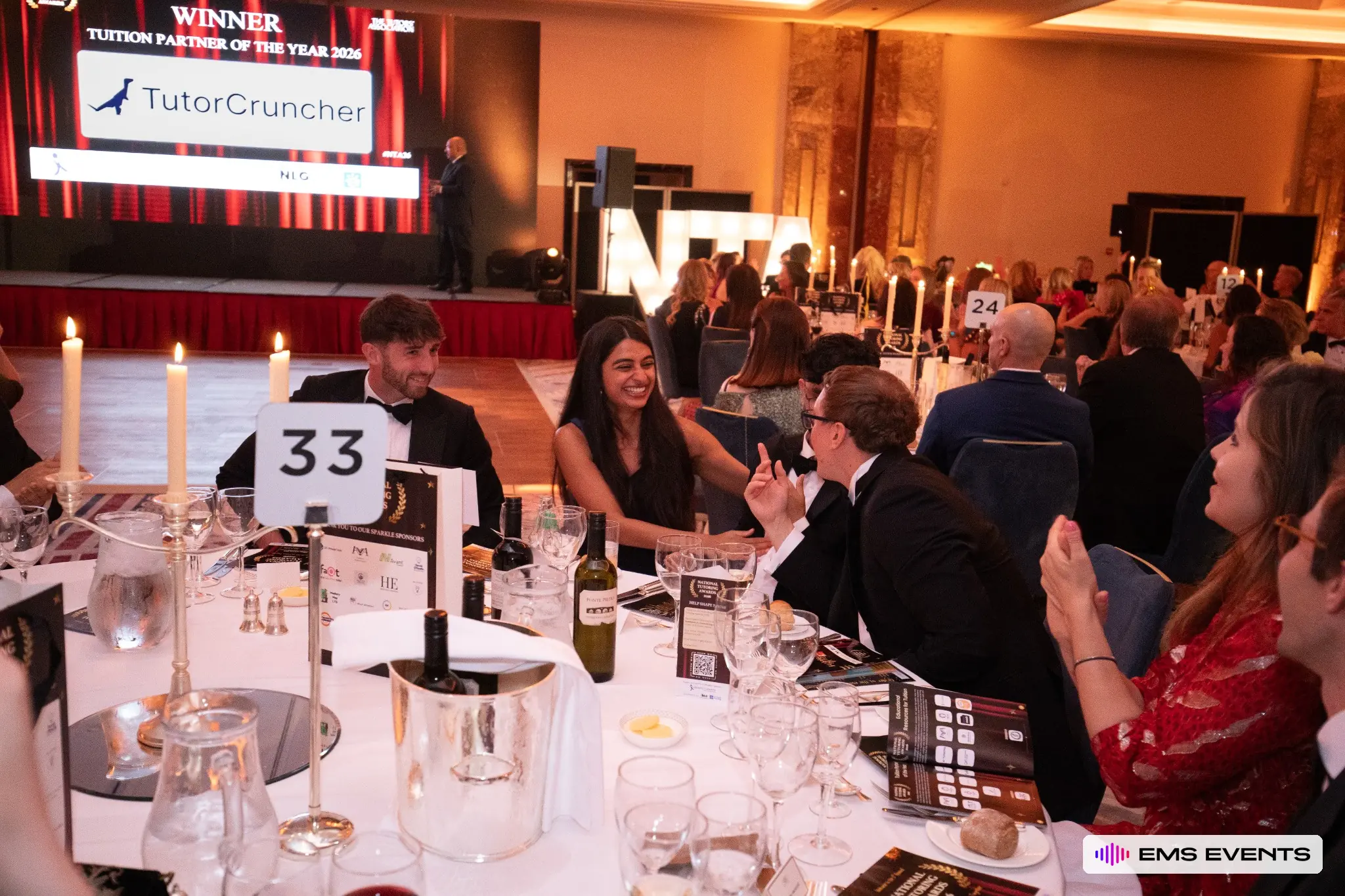 Guests share a moment at their table during the awards ceremony with the winners screen visible behind them