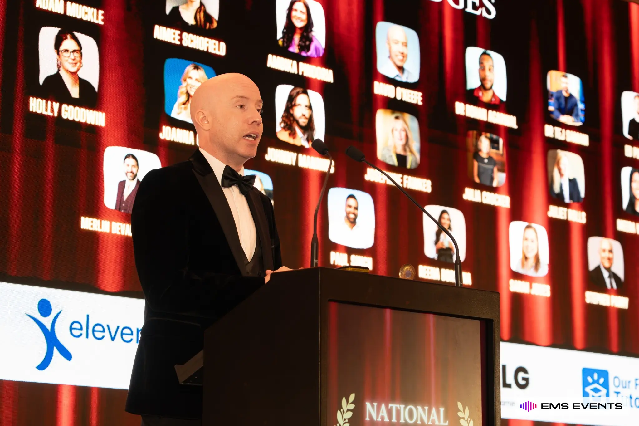 Host at the podium with the judges panel displayed on the LED backdrop at the 5th National Tutoring Awards
