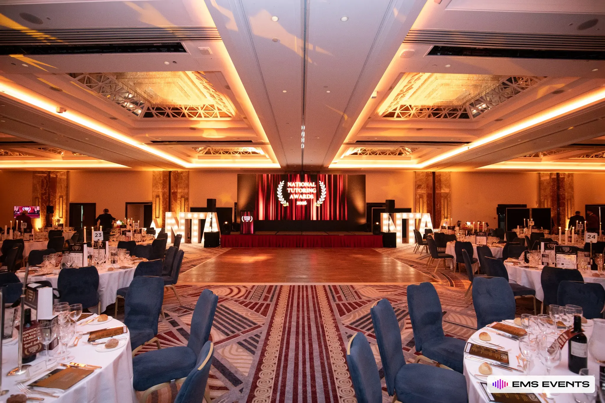 Head-on view of the National Tutoring Awards stage with dance floor, red-skirted stage and NTA marquee letters at Royal Lancaster London