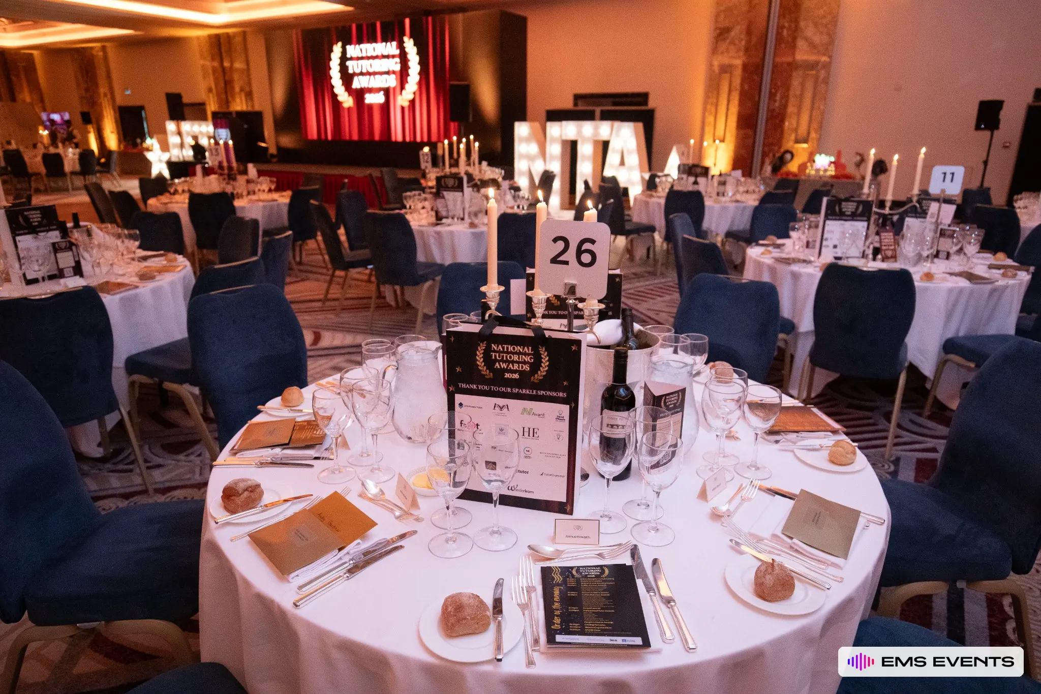 Table centrepiece and NTA 2026 branded sponsor bag with the National Tutoring Awards stage in the background