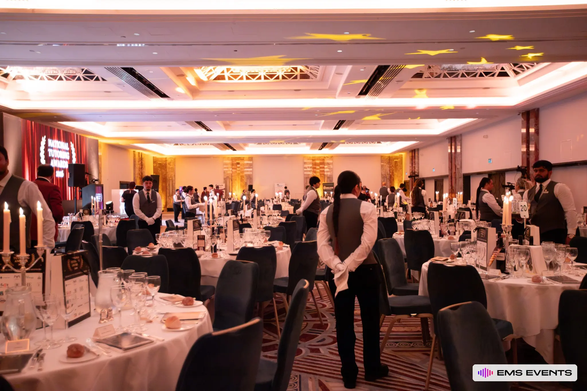 Waiting staff in position with star gobo lighting projected on the ceiling ahead of the National Tutoring Awards