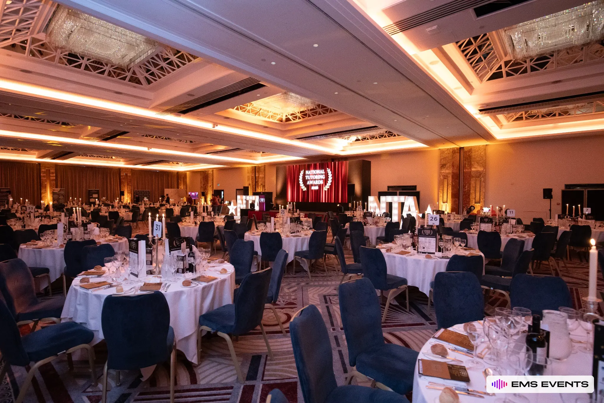 Warm amber uplighting and banquet setup for the National Tutoring Awards ceremony at Royal Lancaster London