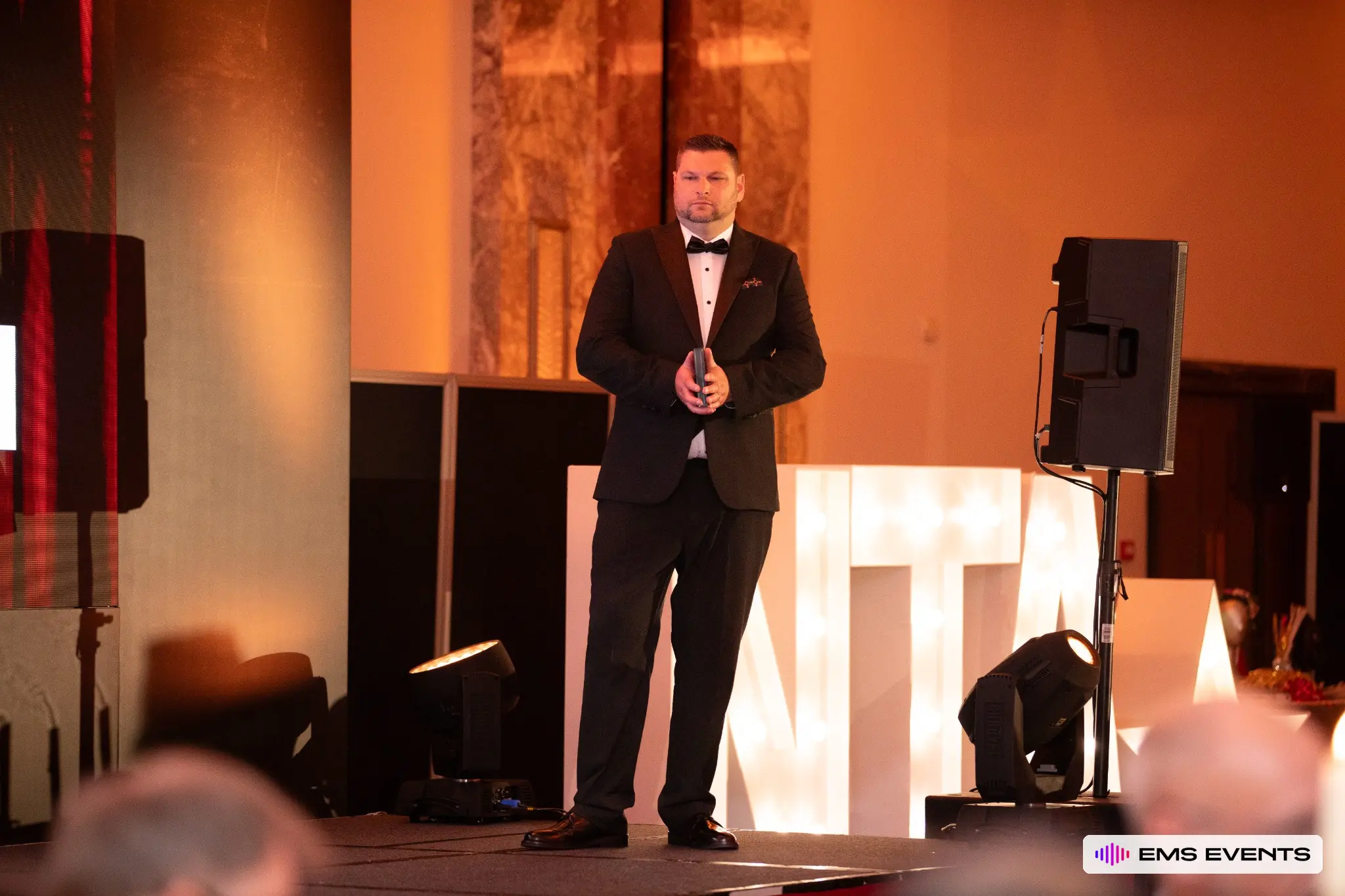 Winner standing on stage with award beside the illuminated NTA marquee letters at the 5th National Tutoring Awards